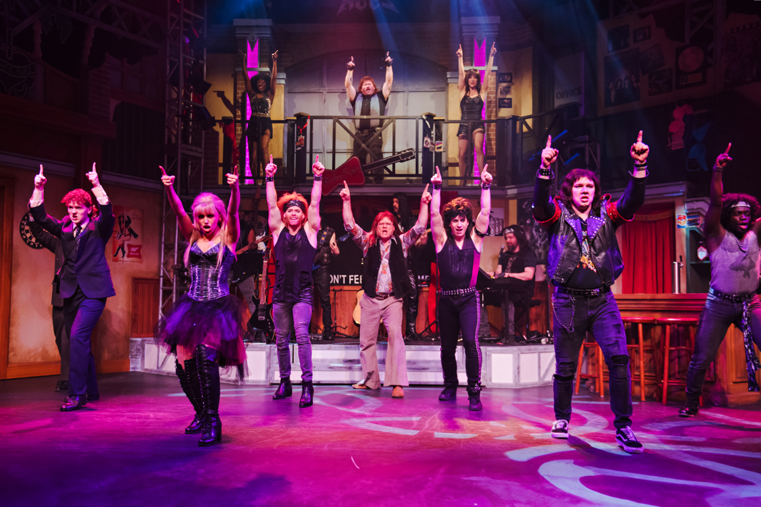 Production photo of Rock of Ages, showing the entire company dancing on stage with dramatic lighting.