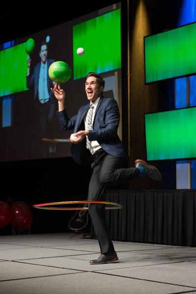 A male juggler, dressed in black with a blue belt, skillfully juggling with dramatic lighting enhance the theatrical energy.