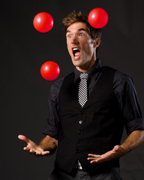 A male juggler, juggling three red balls, dressed in black