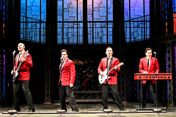 Four actors in red blazers standing in front of microphones and singing.