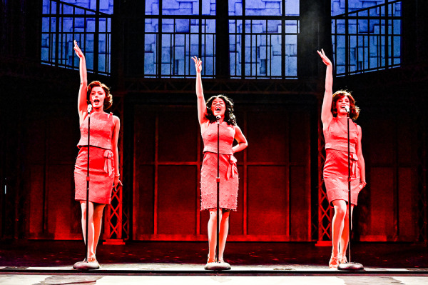 Three actresses in red dresses singing. 