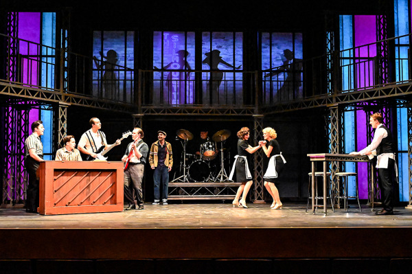 Production photo showing actors playing instruments and dancing on stage.