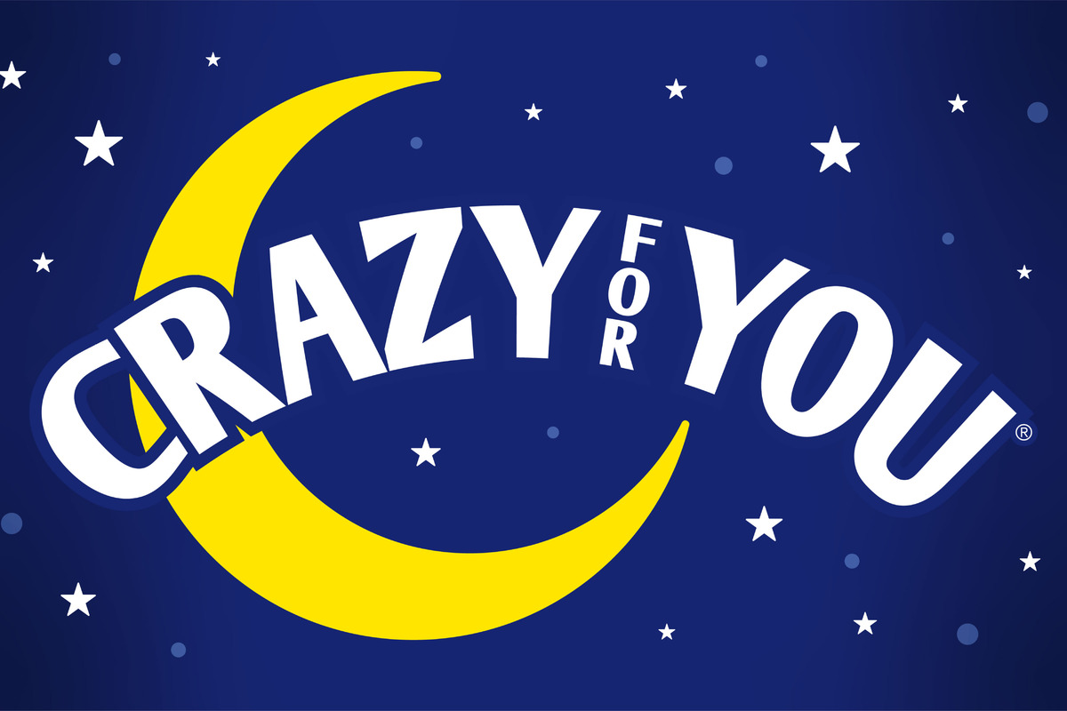 This promotional image for Crazy for You features the title in bold, white letters against a sparkling, bokeh background. The backdrop transitions from warm golden tones at the top to cool blues at the bottom, evoking a lively and festive atmosphere.