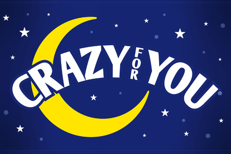 This promotional image for Crazy for You features the title in bold, white letters against a sparkling, bokeh background. The backdrop transitions from warm golden tones at the top to cool blues at the bottom, evoking a lively and festive atmosphere.